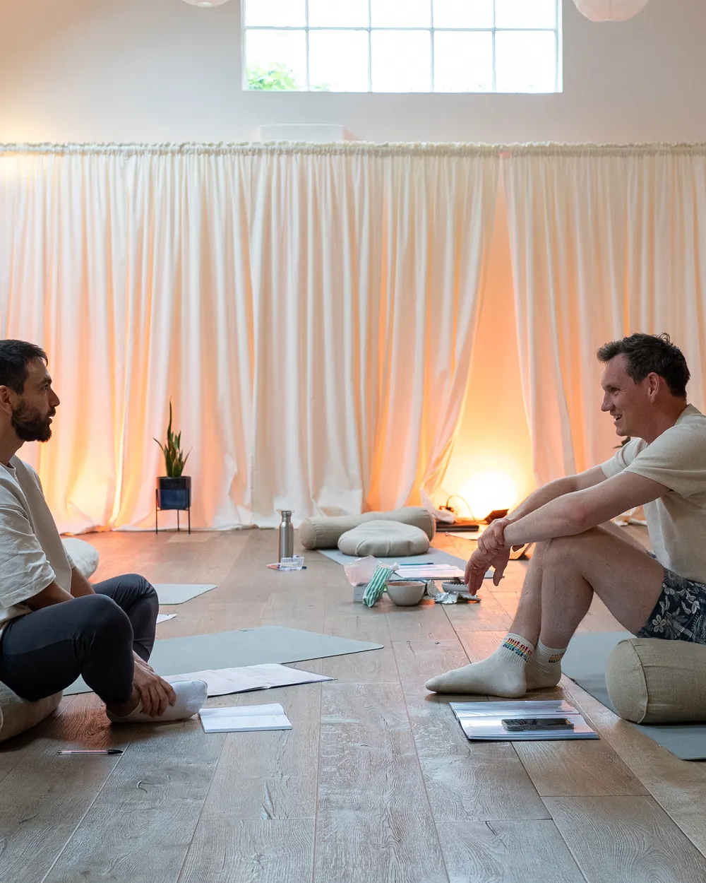 Two men in a facilitator-training session, working through material together on the floor of a sunlit studio