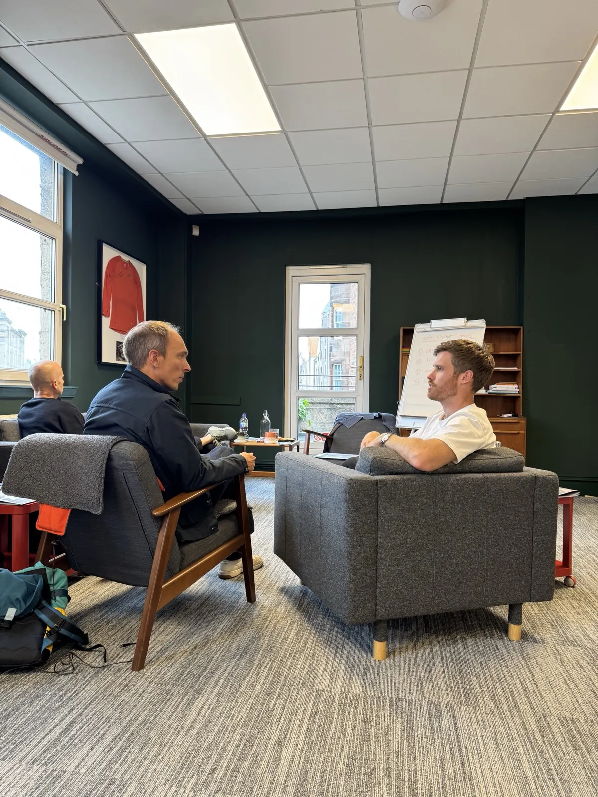 Two trainees in pair work, sitting opposite each other on cushions with window light streaming in behind them